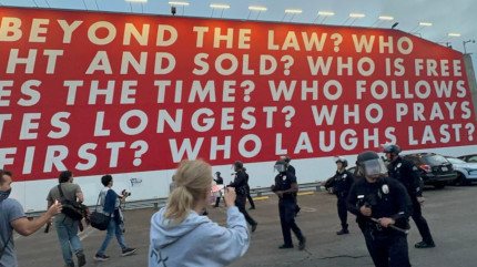 WHO IS 
BEYOND THE LAW? WHO IS BOUGHT AND SOLD? WHO IS FREE TO 
CHOOSE? WHO DOES TIME? WHO FOLLOWS ORDERS? WHO SALUTES 
LONGEST? WHO PRAYS LOUDEST? WHO DIES FIRST? WHO LAUGHS 
LAST? Barbara Kruger mural at the Temporary Contemporary 
behind an apparent confrontation between journalists 
and Law Enforcement in downtown LA a couple days ago