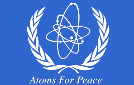 stylized atom centered between white wreaths 
on a field of UN blue, with motto: Atoms For Peace